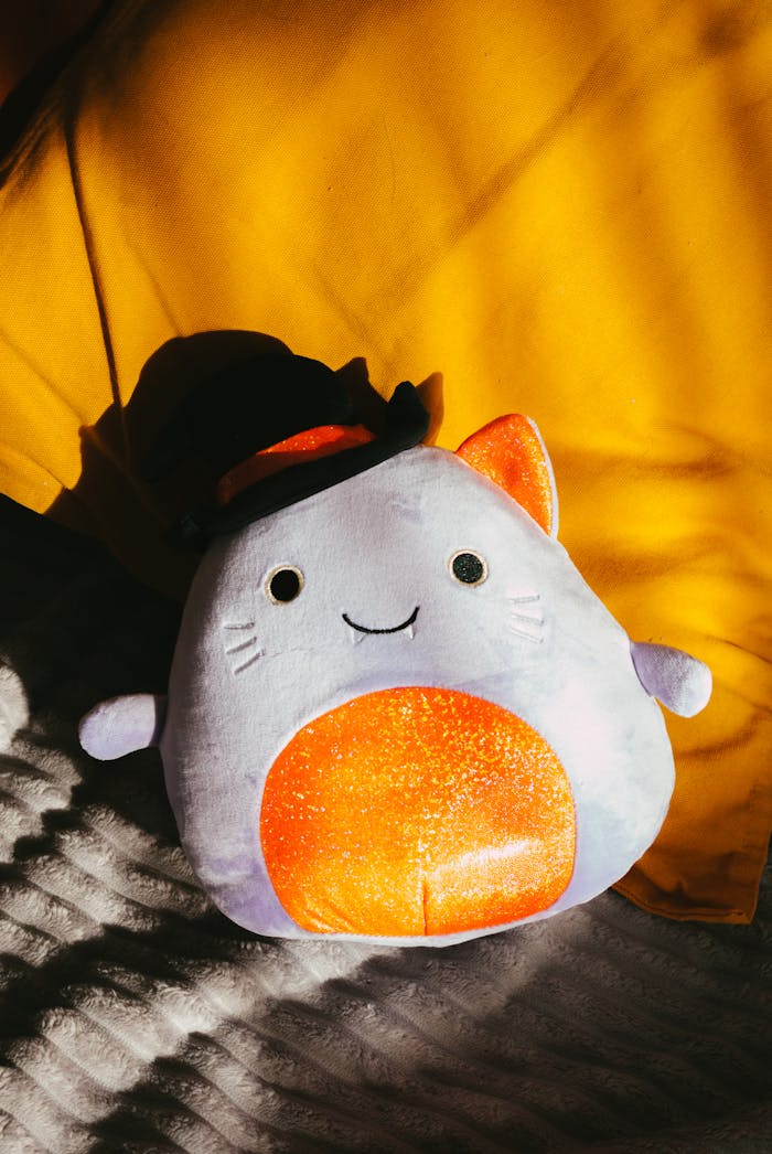 Contact Cute plush cat toy sunlit on yellow and white bedding. Perfect for cozy or playful home decor.